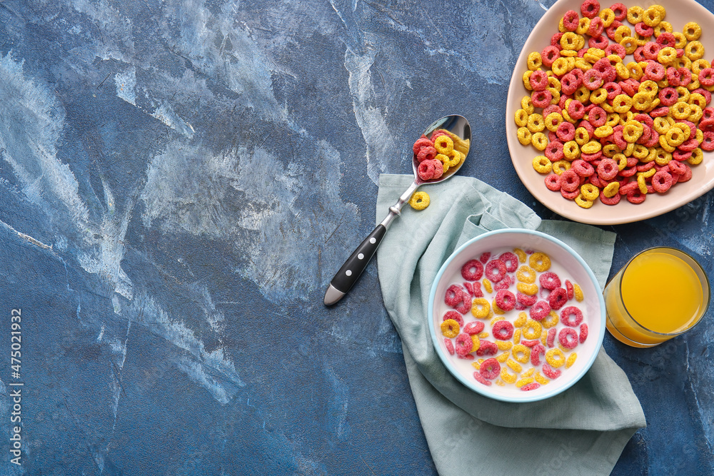 Bowls with colorful cereal rings and glass of juice on color background