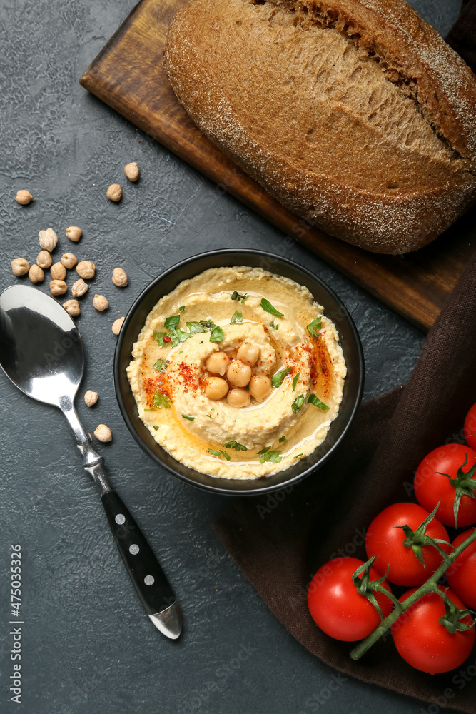 Bowl with delicious hummus, bread and tomatoes on dark background