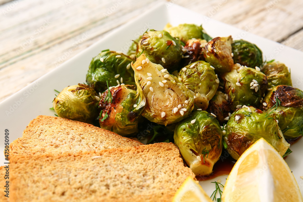 Plate with tasty roasted Brussels cabbage, toasts and lemon on table, closeup