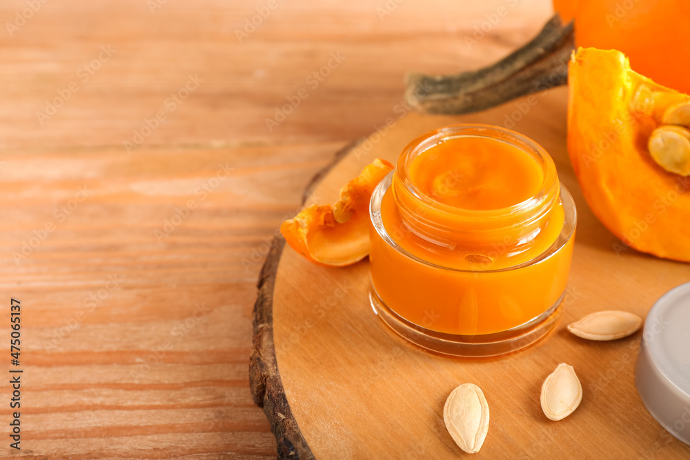 Board with jar of natural pumpkin mask on wooden background, closeup