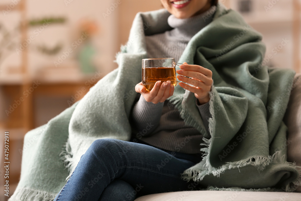 Young woman drinking tasty tea on sofa at home, closeup