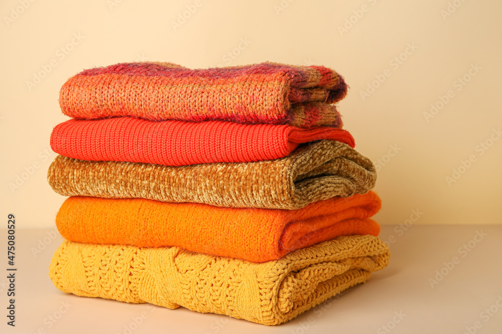 Stack of different stylish sweaters on table against color background