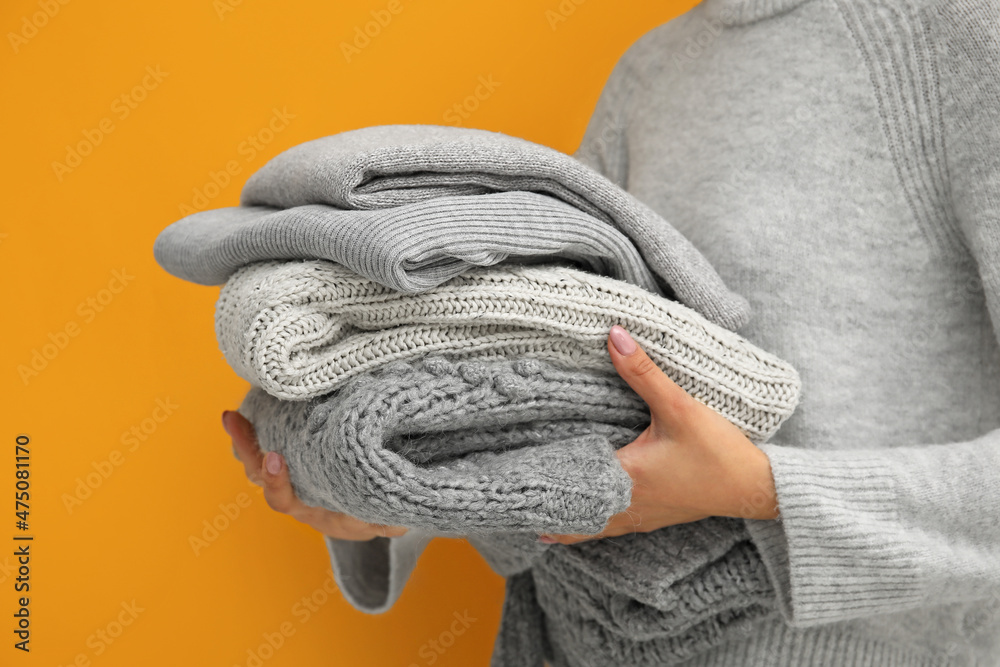 Woman holding stack of stylish sweaters on color background