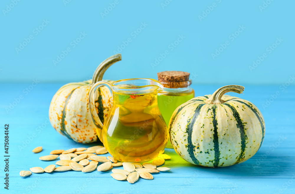 Jug and bottle with pumpkin seed oil on blue background