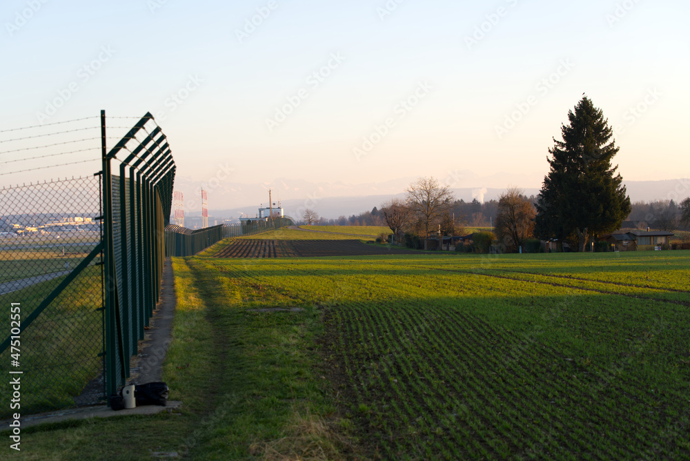 Fence at Zürich Airport on a sunny winter late afternoon with colorful winter sky and Swiss Alps in 