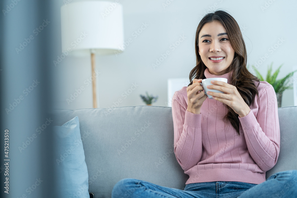 亚洲年轻女性在家里喝咖啡，看电视电影。