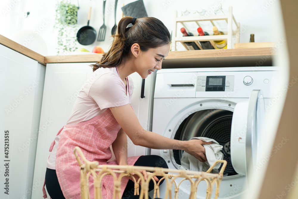 Asian beautiful woman put dirty clothes to washing machine in house.