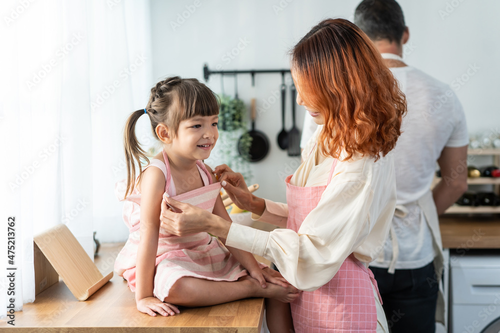 Asian beautiful young mother tying apron for baby kid before cooking.