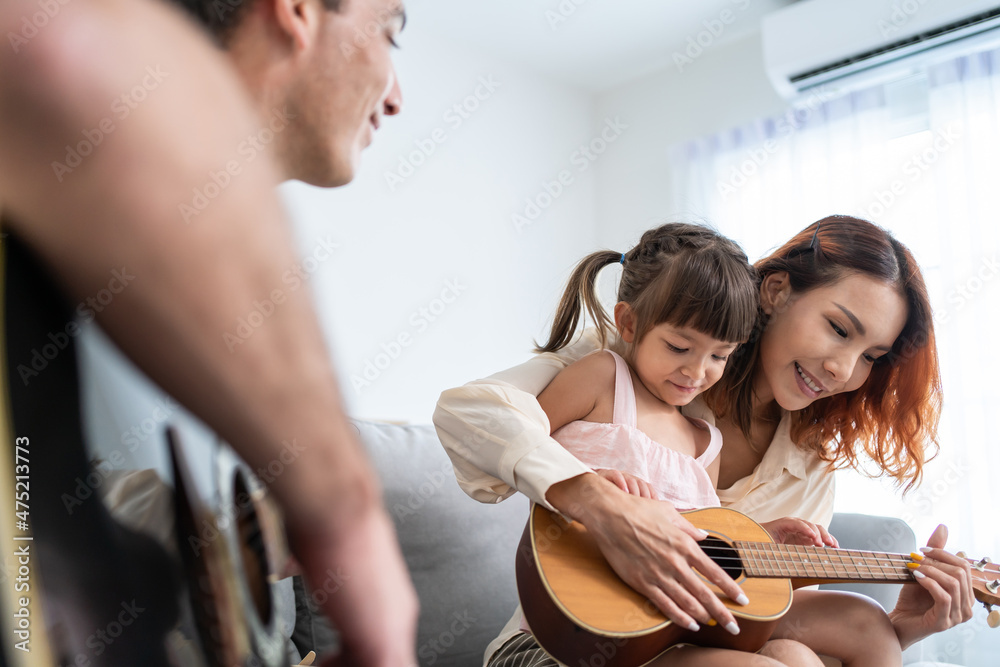 亚洲年轻夫妇在家和年幼的孩子一起弹吉他