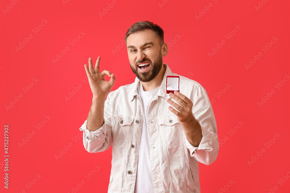 Young man with engagement ring showing OK on color background