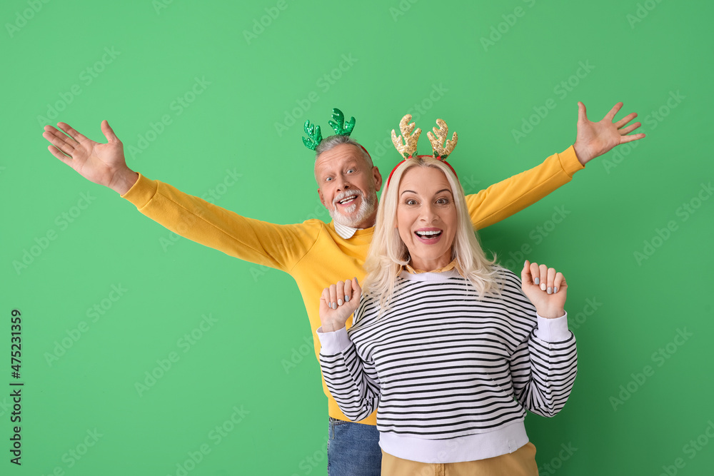 Happy mature couple wearing deer horns on color background