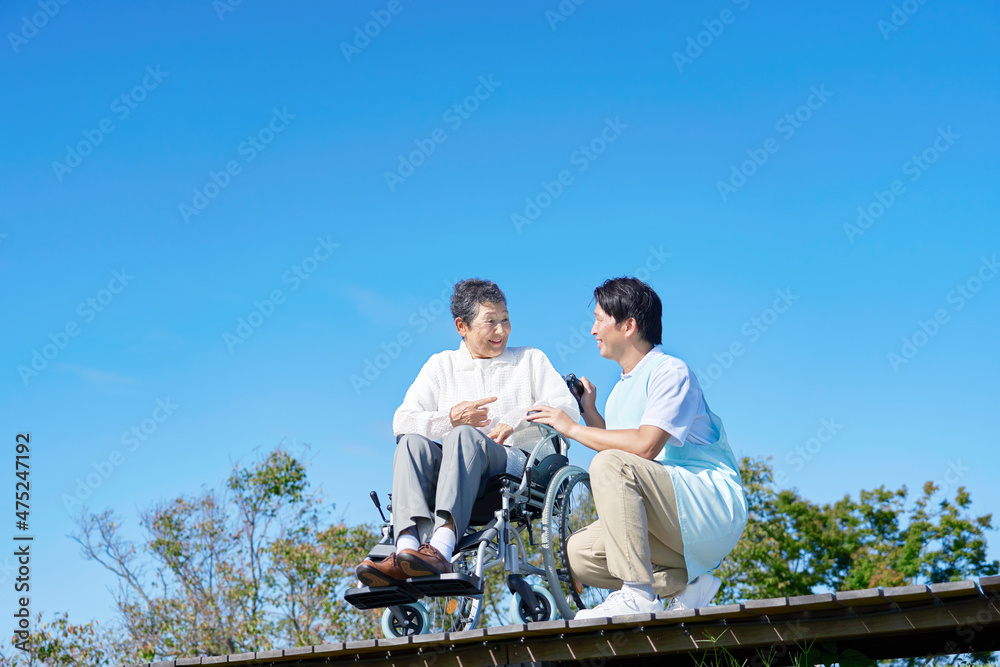 介護士と車椅子に乗る高齢者　屋外