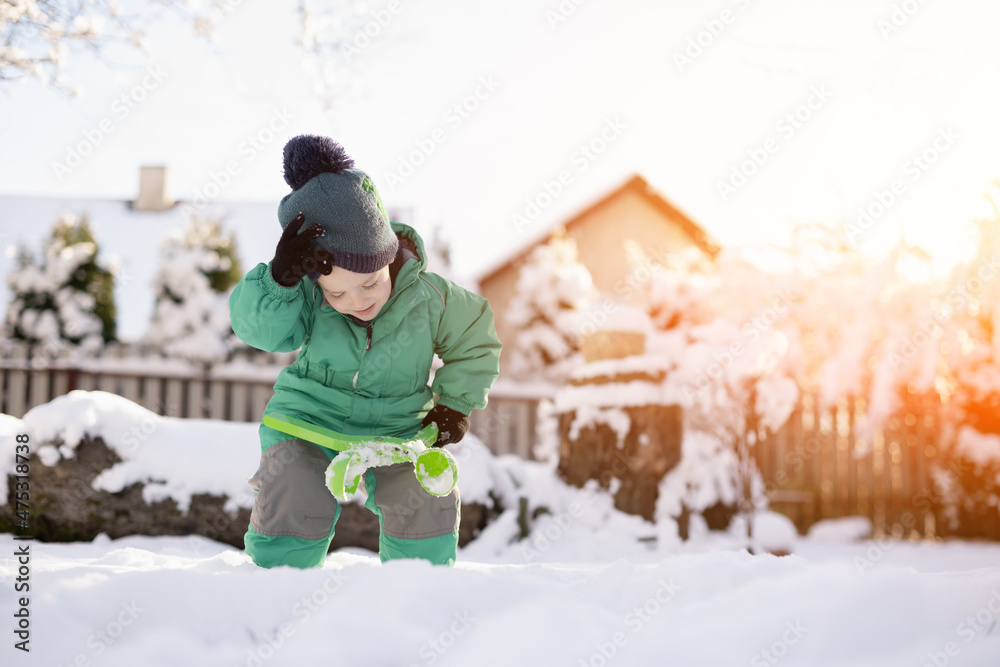 冬天玩雪的男孩。穿着绿色夹克和针织帽子的小孩在ho附近做雪球