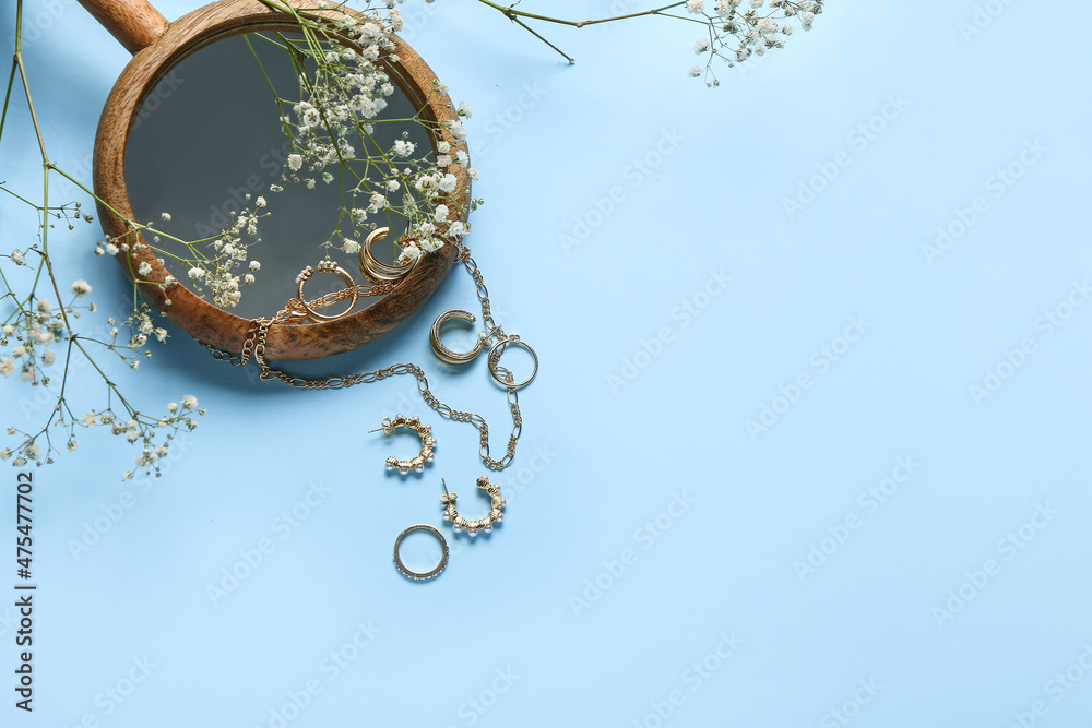 Stylish golden jewelry, mirror and gypsophila flowers on color background