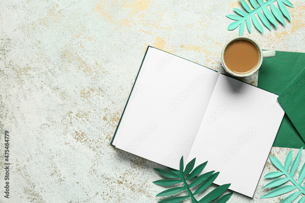 Cup of tasty coffee, blank book and paper leaves on light background