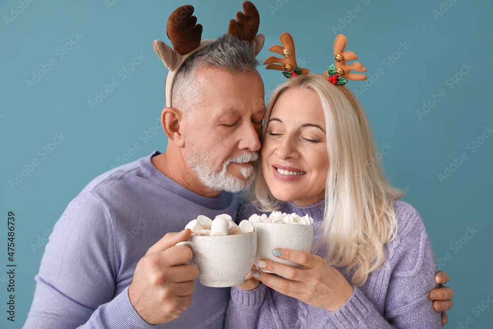 Happy mature couple with hot chocolate on color background