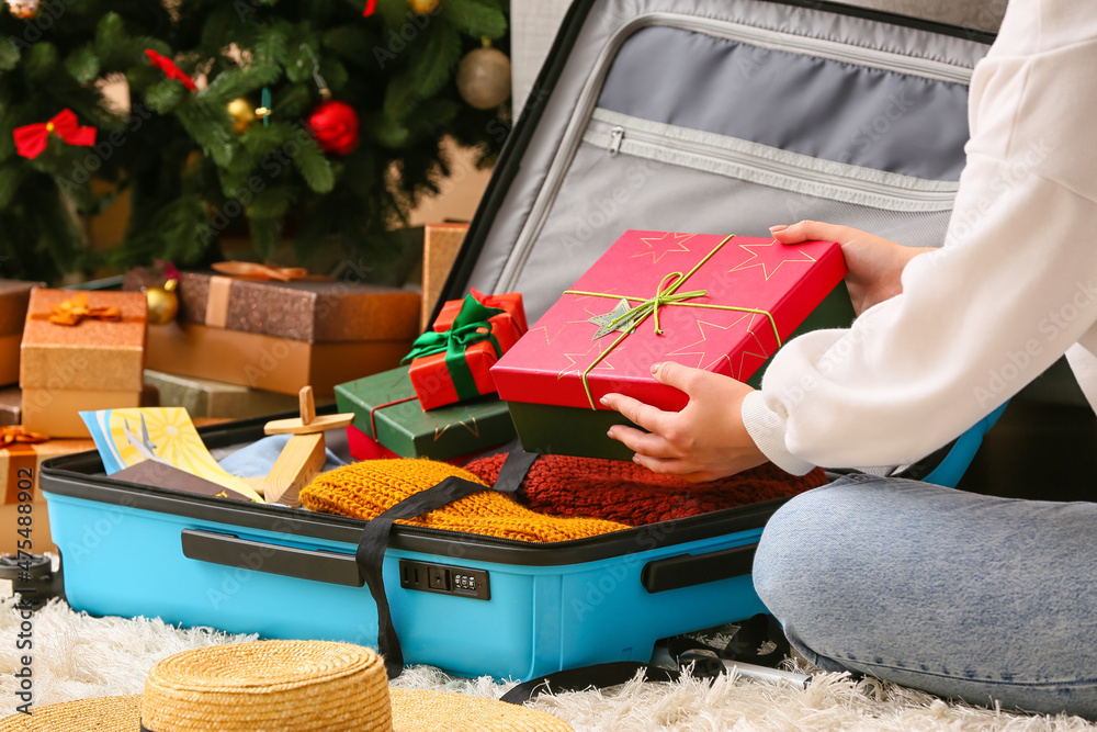 Woman packing Christmas gift boxes in suitcase at home