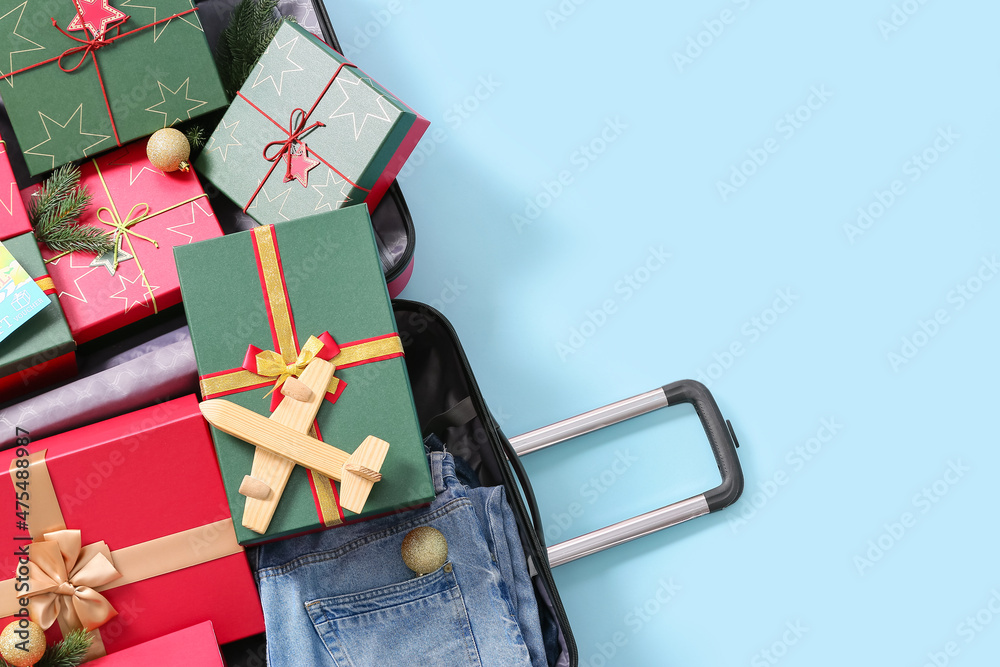 Open suitcase with wooden airplane and Christmas gift boxes on blue background