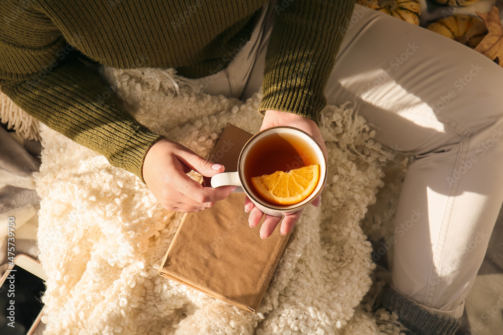 Woman with book holding cup with delicious tea, closeup