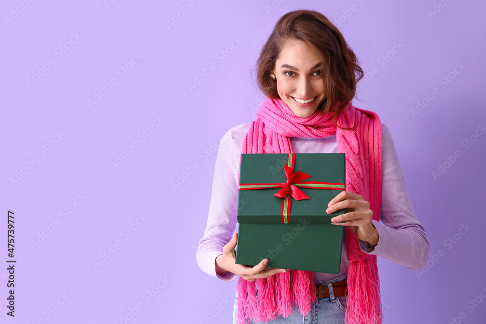 Stylish young woman in winter clothes and with Christmas gift on color background