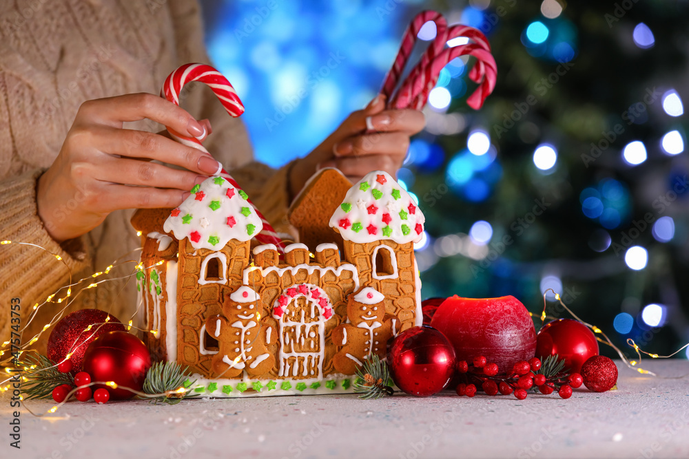 Woman putting treats into gingerbread house at table, closeup