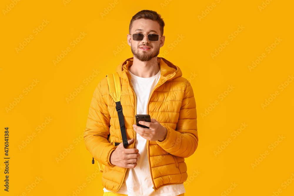 Stylish young man using mobile phone on yellow background