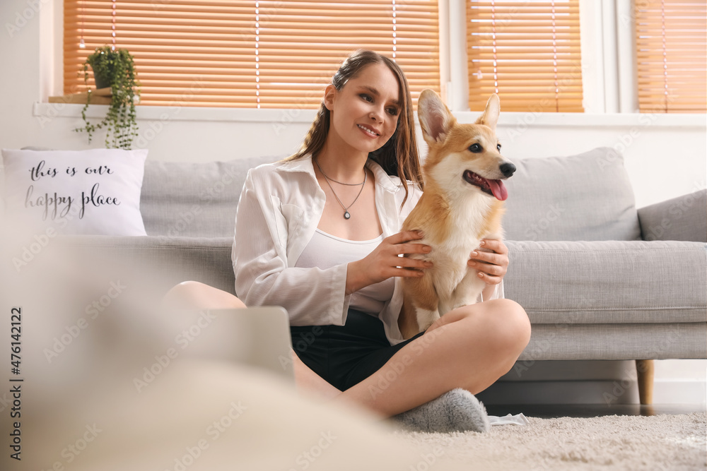 年轻女子带着可爱的柯基犬坐在家里的地板上