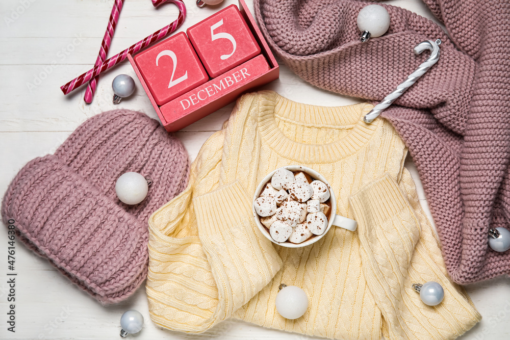 Set of childrens clothes, cup of hot chocolate and calendar with date of Christmas on white wooden 