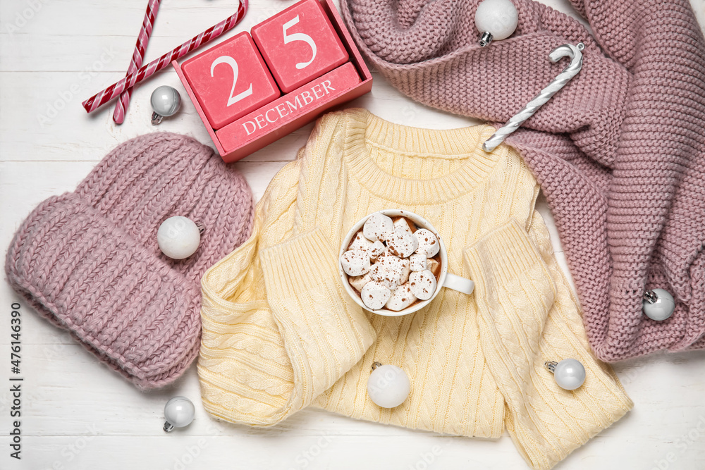 Set of childrens clothes, cup of hot chocolate and calendar with date of Christmas on white wooden 