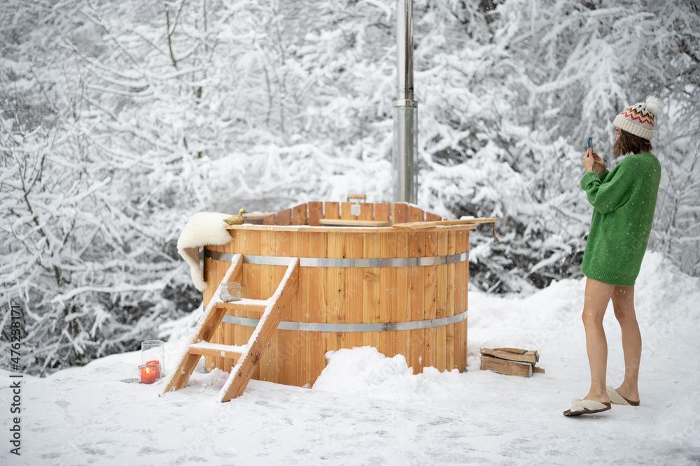 Woman taking photo of a wooden bath, during winter vacations at snowy mountains. Scandinavian lifest