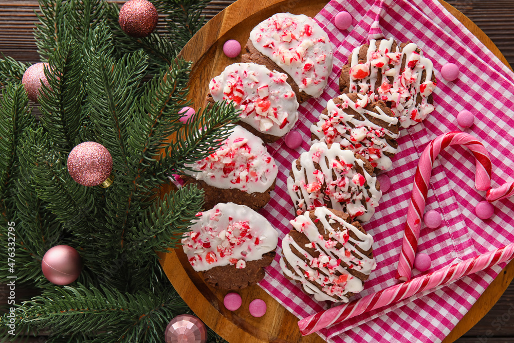 Board with tasty candy cane cookies, fir branch and Christmas balls on dark wooden background, close