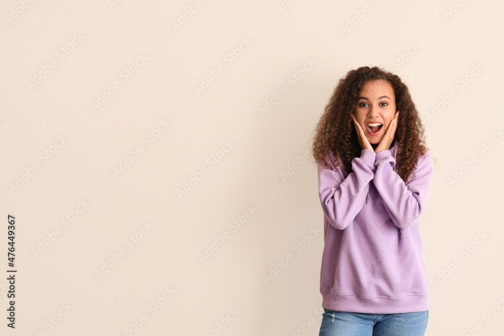 Surprised young African-American woman in stylish hoodie on light background