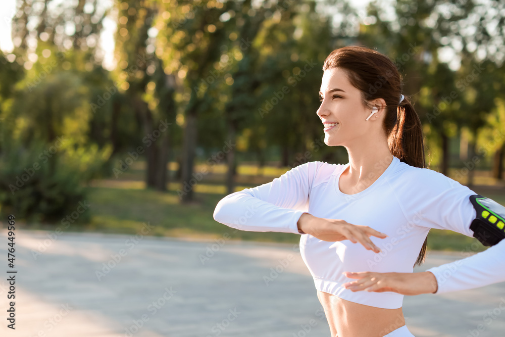 Beautiful young woman with earphones exercising in park