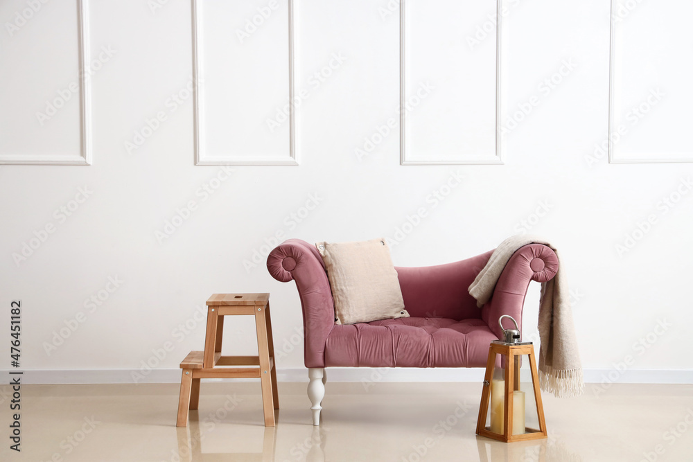 Pink armchair with plaid, stepladder and candles near light wall