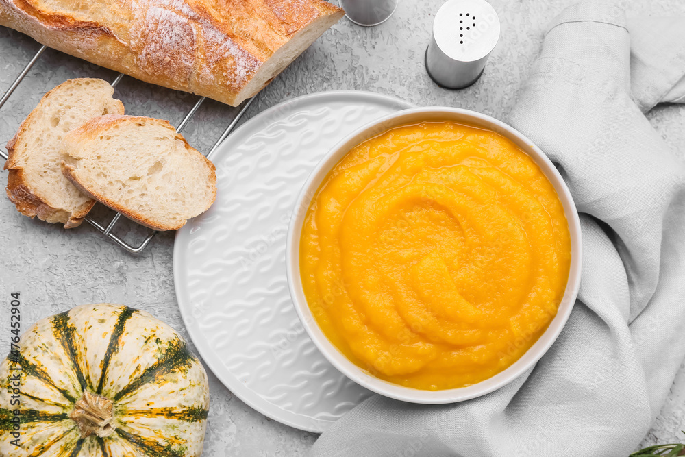 Bowl of tasty pumpkin cream soup and bread on grey background