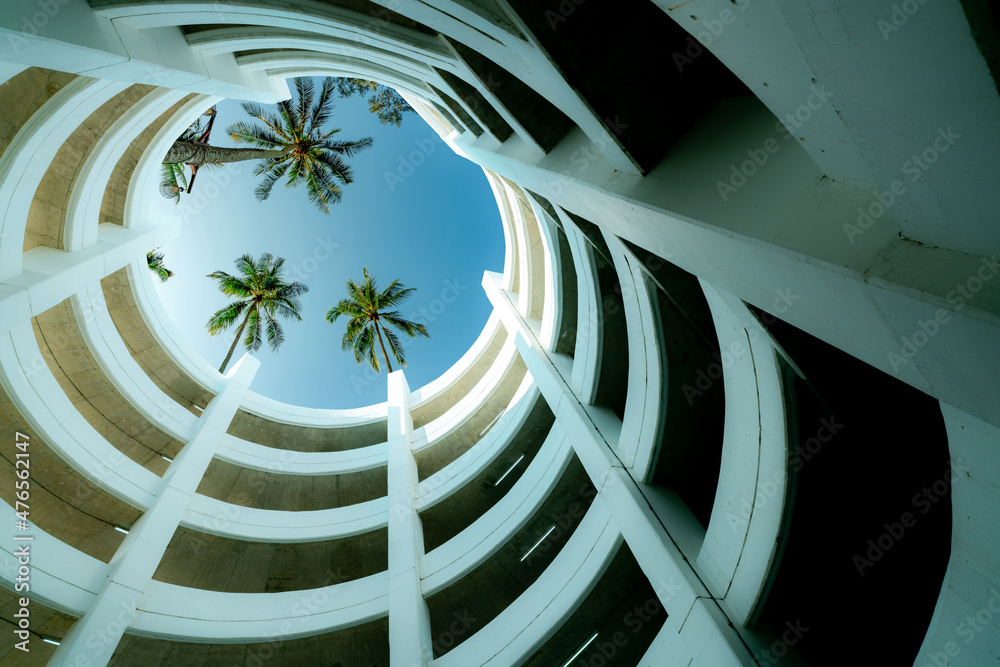 Bottom view multi-story car park building with coconut tree above building in summer. Multi-level pa