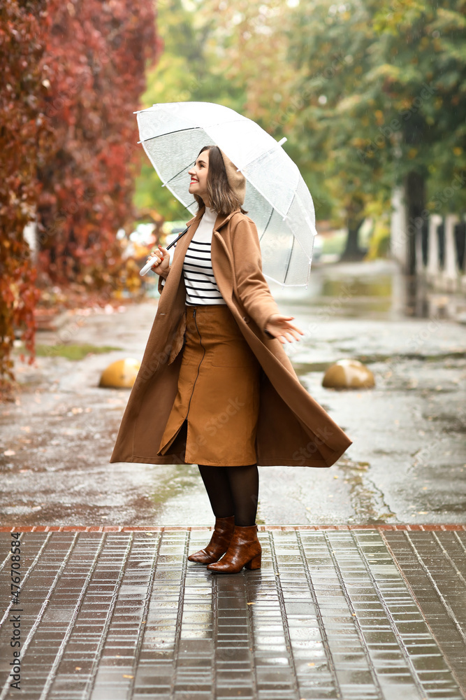 Young woman with umbrella spinning on autumn city street