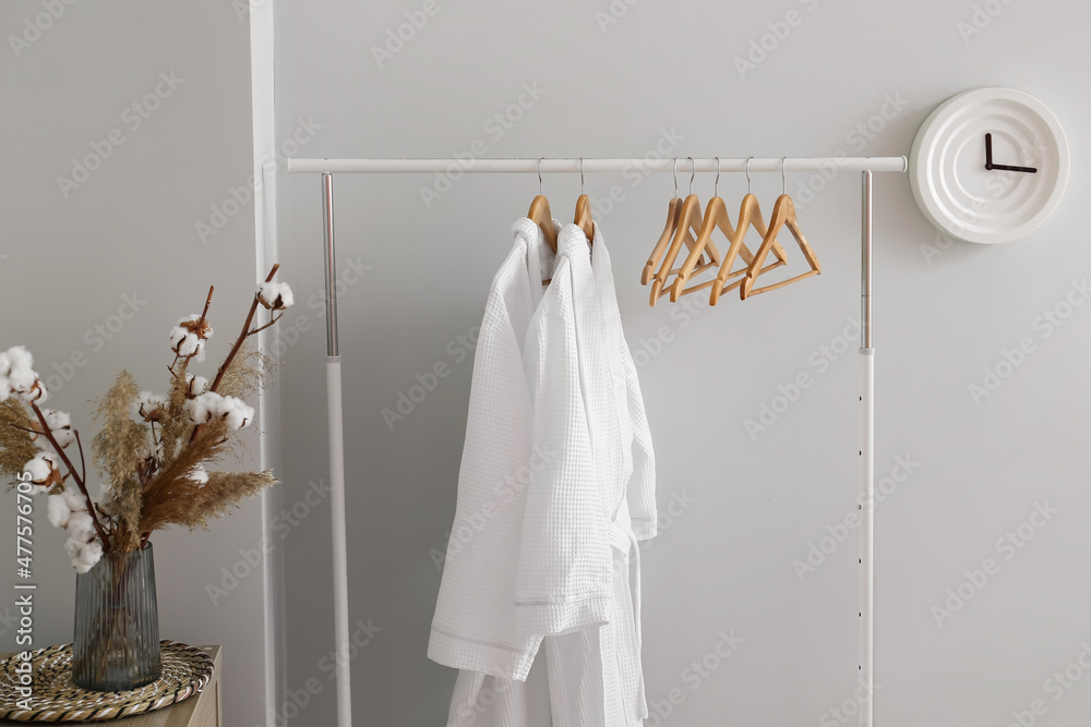 Rack with white bathrobes near light wall in room