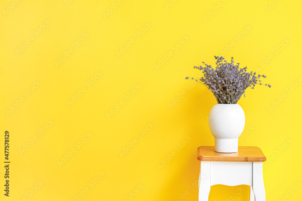 Vase with beautiful lavender flowers on table against color background