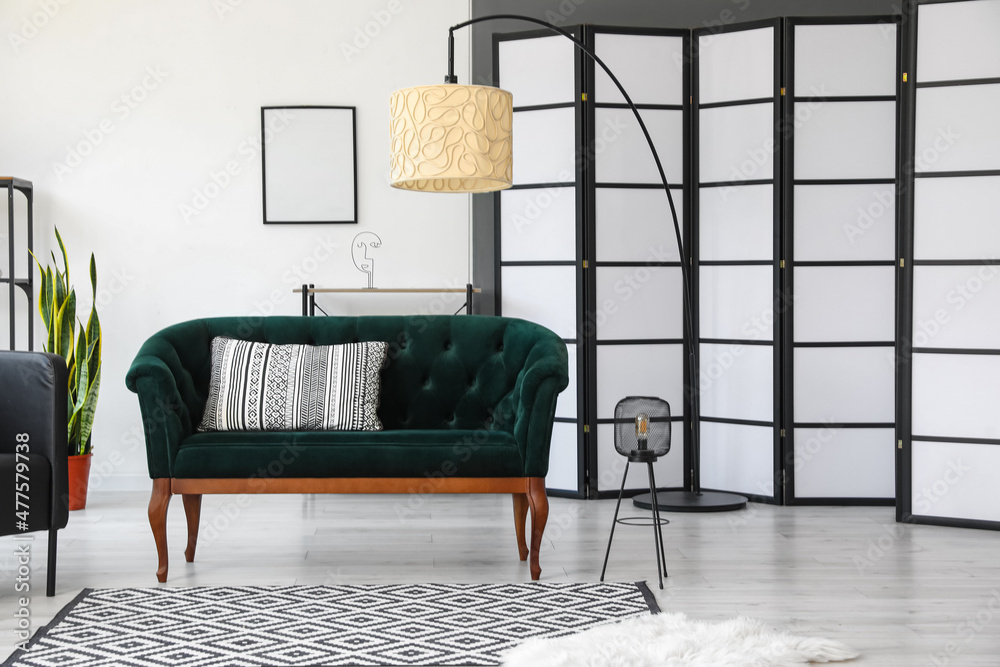 Interior of light living room with green sofa, lamps and folding screen