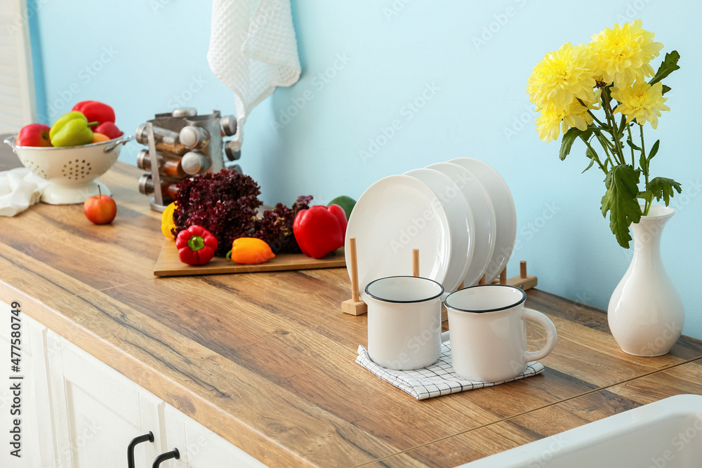 Vase with flowers, cups and plates on wooden table top near blue wall