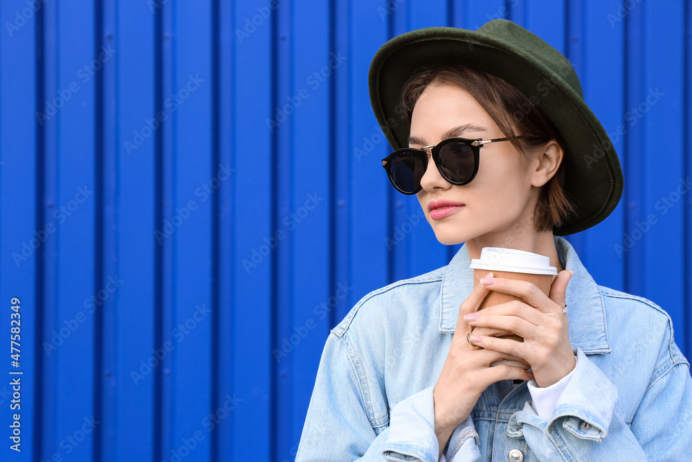 Fashionable woman holding paper cup of tea on blue background