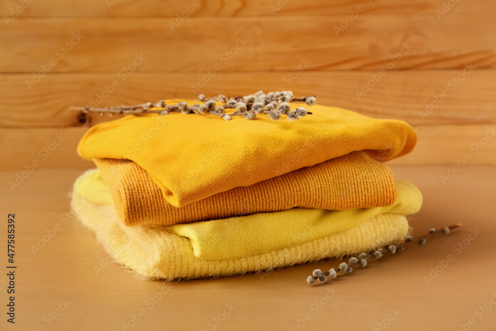 Stack of different cozy sweaters and willow branches on wooden background