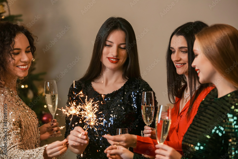 Beautiful young women with sparklers and glasses of champagne celebrating Christmas at home