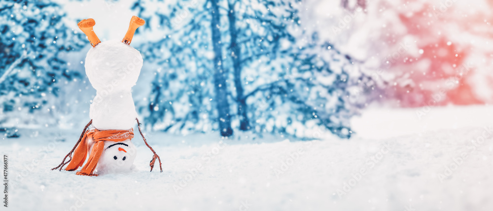 Cheerful snowman with orange scarf and in yellow boots stands upside down in winter