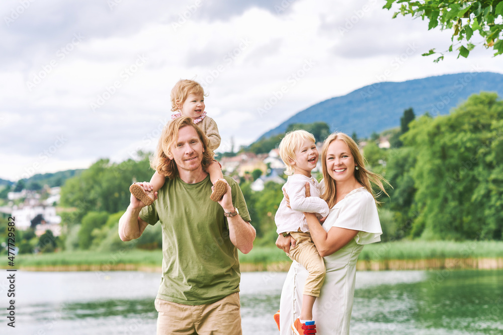 Outdoor portrait of beautiful family, young couple with preschooler boy and toddler girl posing next