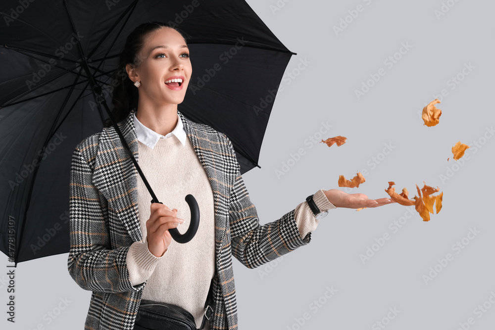 灰色背景下带着雨伞和秋叶的感性女人