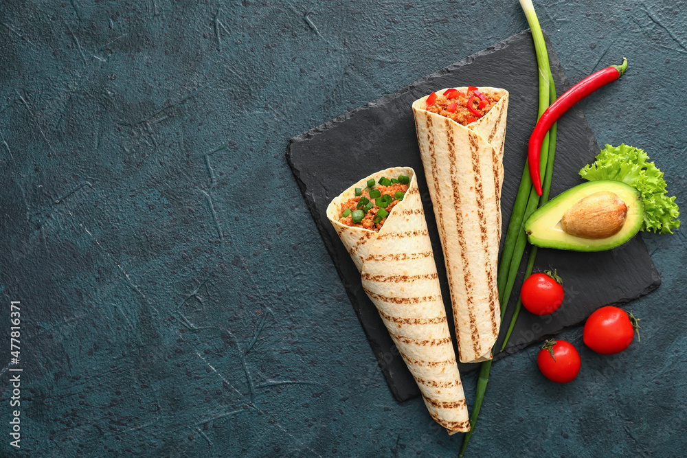 Slate plate with tasty burritos and vegetables on dark background