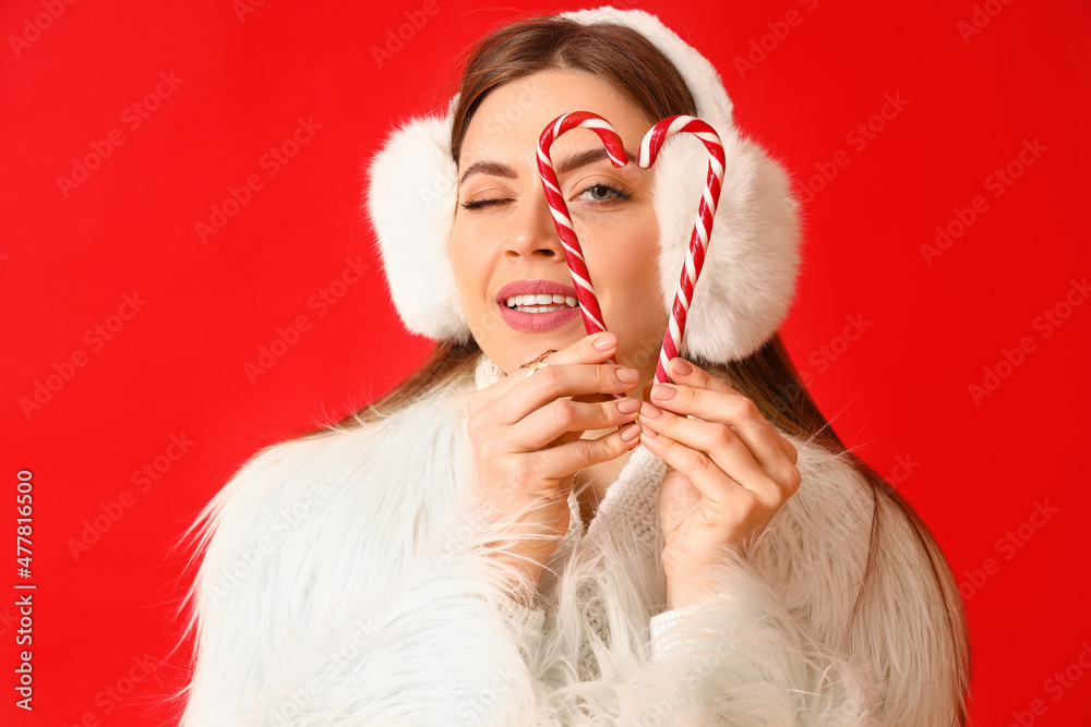 Beautiful young woman in warm winter clothes and with candy canes on color background