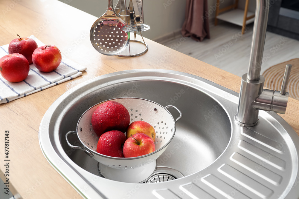 Colander with fresh apples in silver sink